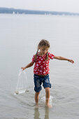 Girl (4-5 years) looking for shells in the lake, Lake Ammersee, Bavaria, Germany