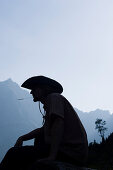 Mann mit Cowboyhut kaut auf einem Grashalm, Lenggries, Oberbayern, Bayern, Deutschland