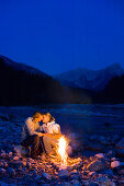 Young couple sitting in front of a camp fire, kissing, Lenggries, Upper Bavaria, Bavaria, Germany