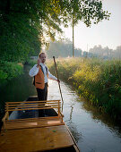 Traditional Spreewald boat in the morning, tourguide Hagen Conrad punting on a stream to pick up tourists in Burg-Kauper, Upper Spreewald, biosphere reservat, Spreewald, Brandenburg, Germany