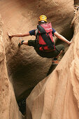 Female canyoneer stemming across a sandstone slot in Pritchett Canyon near Moab, Utah, USA