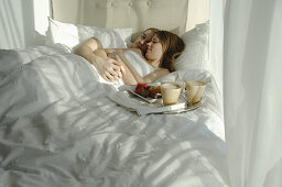 Young couple in bed cuddling with tray of breakfast foods