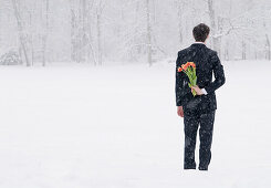 Businessman in a snowstorm hiding bouquet of tulips behind his back, English garden, Munich, Bavaria, Germany