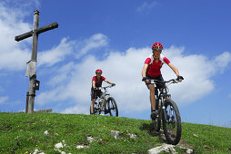 Couple with mountainbikes near summit cross, Wendelstein range, Bavarian foothills, Bavaria, Germany
