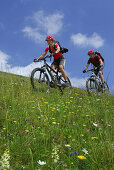 Zwei Mountainbiker fahren über Almwiese, Bayerische Voralpen, Oberbayern, Bayern, Deutschland