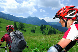 Junge Frau und Mann beim Mountainbiken über Almwiese, Wendelsteinregion, Bayerische Voralpen, Bayerische Alpen, Oberbayern, Bayern, Deutschland