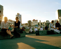 Menschen sitzen an der Hafenpromenade im Licht der Abendsonne, City-to-Sea-Bridge, Wellington, Nordinsel, Neuseeland