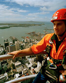 Young man with climbing equipment on top of Sky Tower, view at Central Business District and Waitemata Harbour, Auckland, North Island, New Zealand