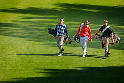 Three golfers walking over golf course, Strasslach-Dingharting, Bavaria, Germany