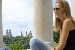 Young woman sitting at Monopteros, Church of our lady and  Theatine Church, Englisch Garden, Munich, Bavaria, Germany