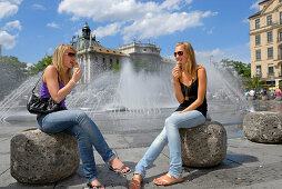 Zwei junge Frauen beim Eisessen vor Springbrunnen am Stachus, Karlsplatz, München, Oberbayern, Bayern, Deutschland