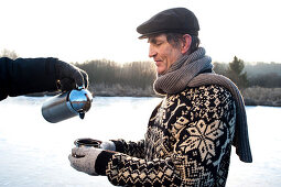 Person pouring tea into cup of senior man, lake Ammersee, Upper Bavaria, Germany