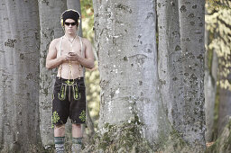 Young man wearing leather trousers standing in a forest, Kaufbeuren, Bavaria, Germany