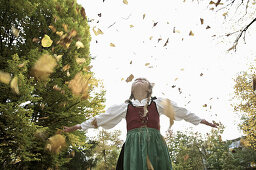 Girl wearing a dirndl, playing in autumn leaves, Kaufbeuren, Bavaria, Germany