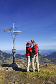 Paar umarmt sich am Gipfelkreuz, Kleiner Traithen, Bayerische Alpen, Bayern, Deutschland