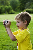 A caucasian boy, 5-10, taking a photograph at a park.
