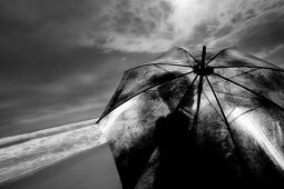 Mujer con paraguas sentada en la playa tras la tormenta. Blanco y Negro.