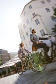 Two businesspeople riding bicycles over cobblestone pavement, Munich, Bavaria, Germany
