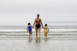 grandmother and two kids walking into the surf at the beach hand in hand