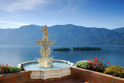 Lago Maggiore mit Isole di Brissago, Insel Brissago, und Monte Gambarogno mit Springbrunnen und Blumenschmuck im Vordergrund, Ronco sopra Ascona, Lago Maggiore, Tessin, Schweiz