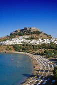 Blick auf Bucht mit Strand, Ort und Akropolis unter blauem Himmel, Lindos, Rhodos, Griechenland, Europa