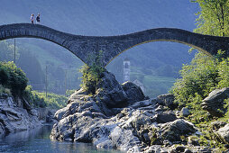 Hikers on the stone bridge Ponte dei Salti at Valle Verzasca, Ticino, Switzerland, Europe