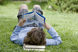 Boy laying on grass reading a book