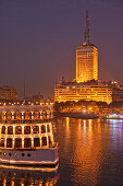 Beleuchtetes Schiff auf dem Nil vor dem Hochhaus des ägyptischen Fernsehsenders, Kairo, Ägypten, Afrika