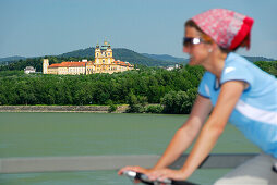 Female cyclist riding along Danube river, Melk abbey in background, Danube Cycle Route Passau to Vienna, Wachau, Lower Austria, Austria