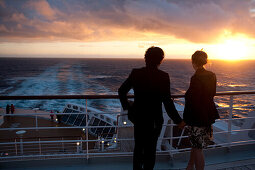 Junges Paar schaut sich den Sonnenuntergang an, Passagiere auf dem Achterdeck, Kreuzfahrtschiff Queen Mary 2, Transatlantik, Nordatlantik, Atlantik