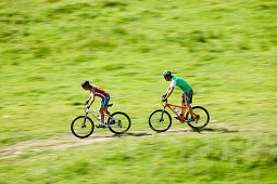 Zwei Mountainbiker fahren über eine Wiese, Spitzingsee, Bayern, Deutschland