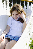 Girl speaking with her mobile phone laying on a hammock in the garden