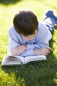 Boy laying on the grass reading a book