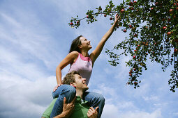 Woman on man's shoulders, reaching for an apple, Styria, Austria