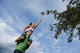 Woman on man's shoulders, reaching for an apple, Styria, Austria