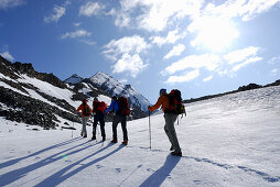 Vier Bergwanderer steigen über ein Schneefeld zum Hochfeiler auf, Zillertaler Alpen, Südtirol, Italien