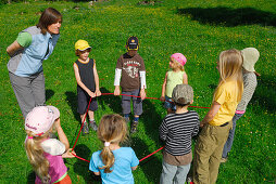 Kinder stehen im Kreis auf einer Wiese, Frau gibt Spielanleitung, Bayerische Alpen, Oberbayern, Bayern, Deutschland
