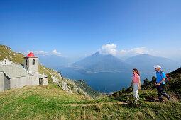 Zwei Wanderer bei der Kapelle San Bernardo, Monti Lariani, Comer See im Hintergrund, Lombardei, Italien