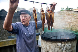 Fisherman hanging fishes into smoke barrel, Utersum, Foehr island, Schleswig-Holstein, Germany