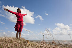 Frau mit ausgebreiteten Armen am Strand von Utersum, Insel Föhr, Schleswig-Holstein, Deutschland