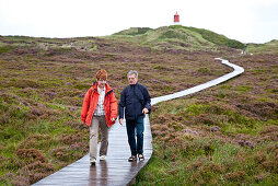 Couple walking along wooden path, lighthouse in background, Amrum island, Schleswig-Holstein, Germany