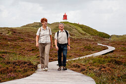 Paar läuft über Bohlenweg, Leuchtturm im Hintergrund, Insel Amrum, Schleswig-Holstein, Deutschland