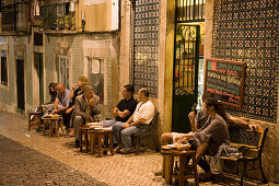 Nachtaufnahme von Menschen vor Alfaia Wein Bar in der Altstadt, Lissabon, Portugal, Europa