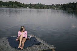 Young woman lying on a jetty while reading a book, lake Starnberg, Bavaria, Germany