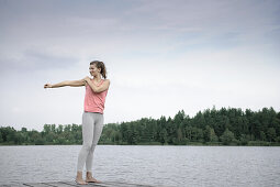 Young woman stretching on a jetty at lake Starnberg, Bavaria, Germany