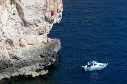 Eine junge Frau und ein junger Mann klettern an den Klippen der Bucht von Zurrieq, in der Nähe ein kleines Schiff, Malta, Europa