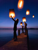 Three persons holding Sky lanterns, Lake Chiemsee, Bavaria, Germany