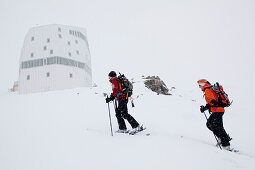 Two female back country skiers in snowstorm, Monte Rosa Hut in background, Canton of Valais, Switzerland