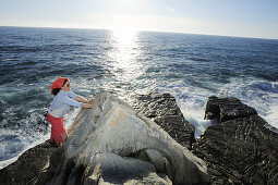 Frau klettert an Fels direkt an der Mittelmeerküste, Ligurien, Italien