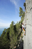 Woman climbing a steep rock face at the Mediterranean, natural park Porto Venere, national park Cinque Terre, UNESCO world heritage site, Liguria, Italy